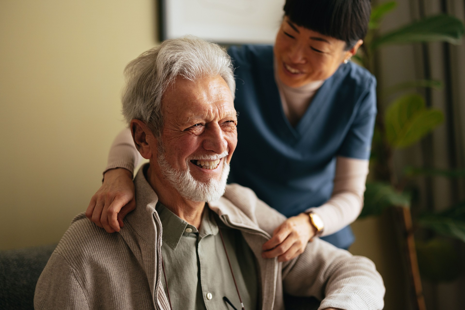 Portrait of a Smiling Elderly Man Taking a Jacket off With a Help of a Woman in a Care Home